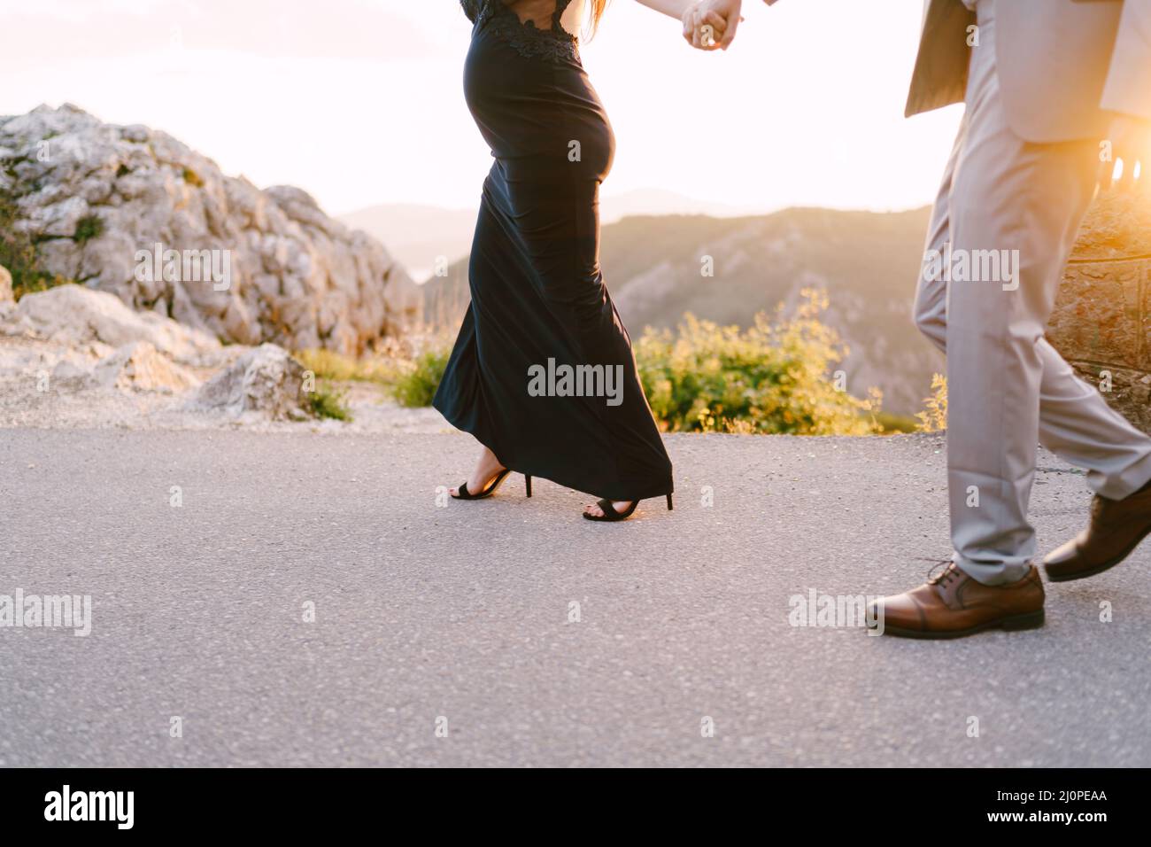 Mann und eine Schwangere gehen auf einer asphaltierten Straße in den Bergen. Nahaufnahme Stockfoto