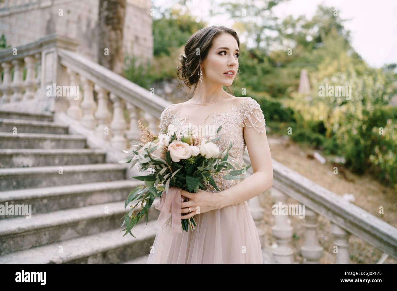 Braut mit einem Blumenstrauß auf Steintreppen im Garten in der Nähe der alten Villa Stockfoto