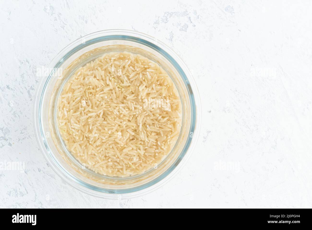 Brauner Reis in Wasser einweichen, um Getreide zu gären und die Phytsäure zu neutralisieren. Stockfoto