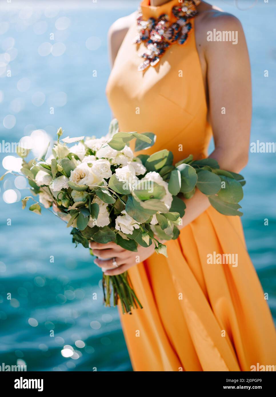 Frau in einem gelben Kleid mit einem Blumenstrauß steht vor einem Hintergrund aus Wasser. Nahaufnahme Stockfoto