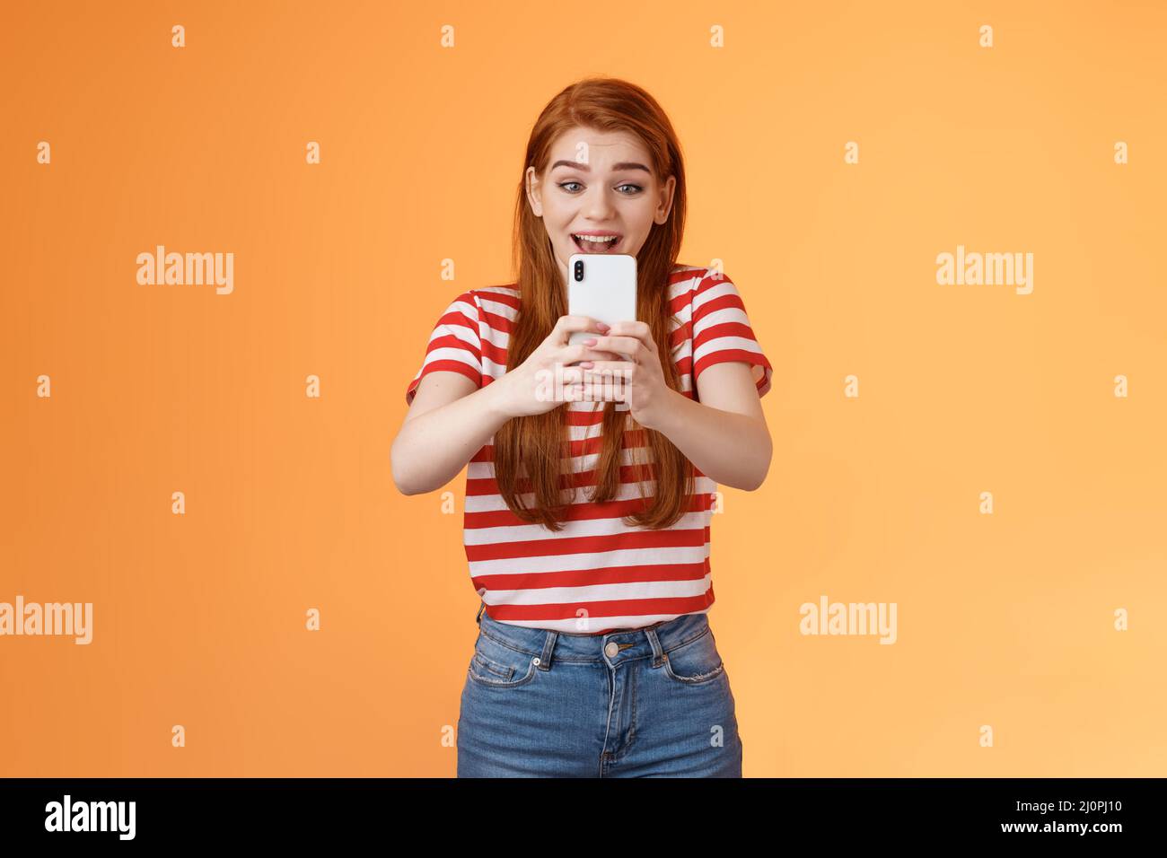 Aufgeregt Mädchen Aufnahme Video halten Smartphone Blick durch Handy Kamera schießen begeistert tolle Leistung. Niedliche Rothaarige Stockfoto