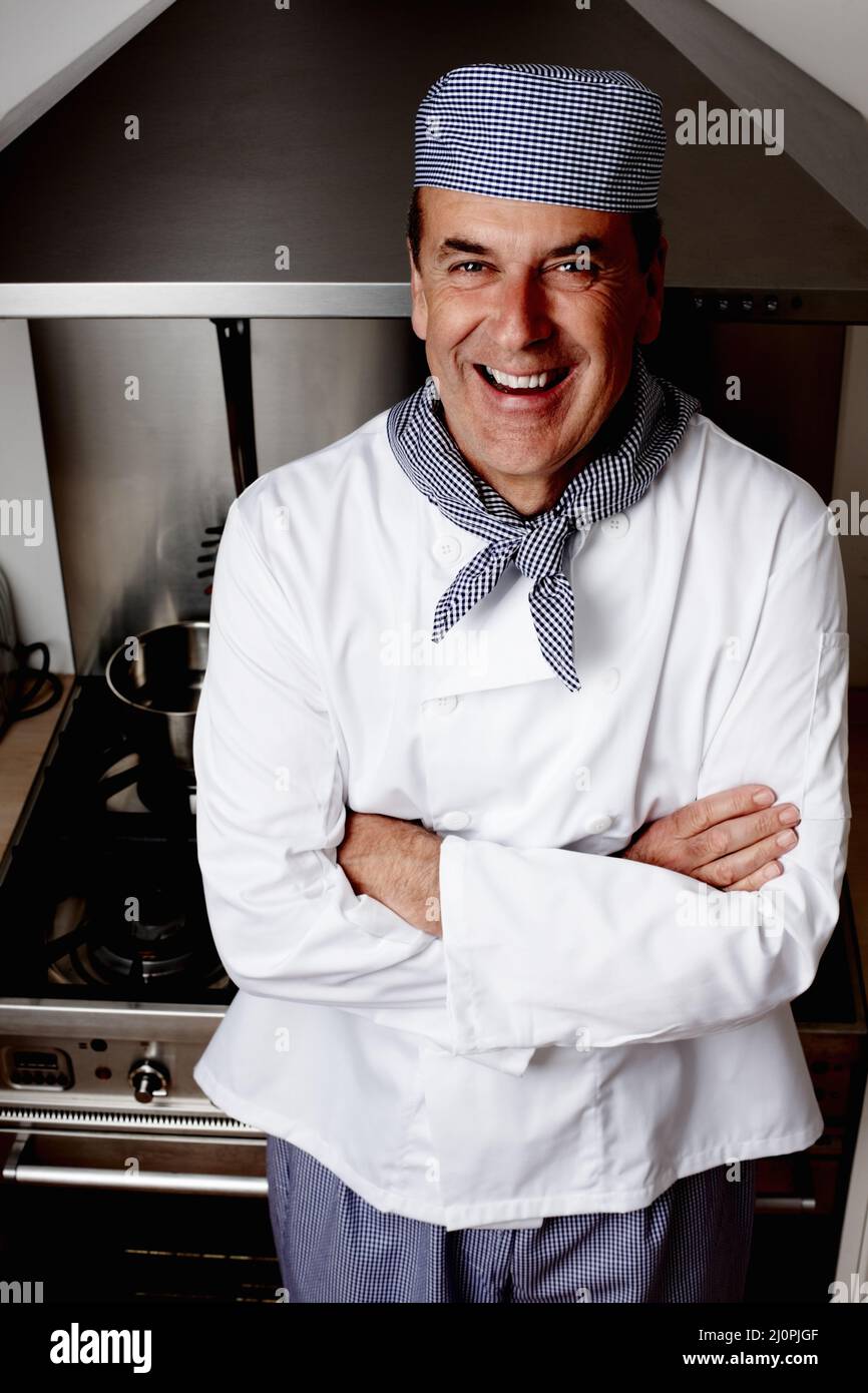 Chefkoch mit gefalteten Händen, die vor der Belüftungshaube stehen. Porträt eines fröhlichen Chefkochs mit gefalteten Händen, die vor der Dunstabzugshaube stehen. Stockfoto