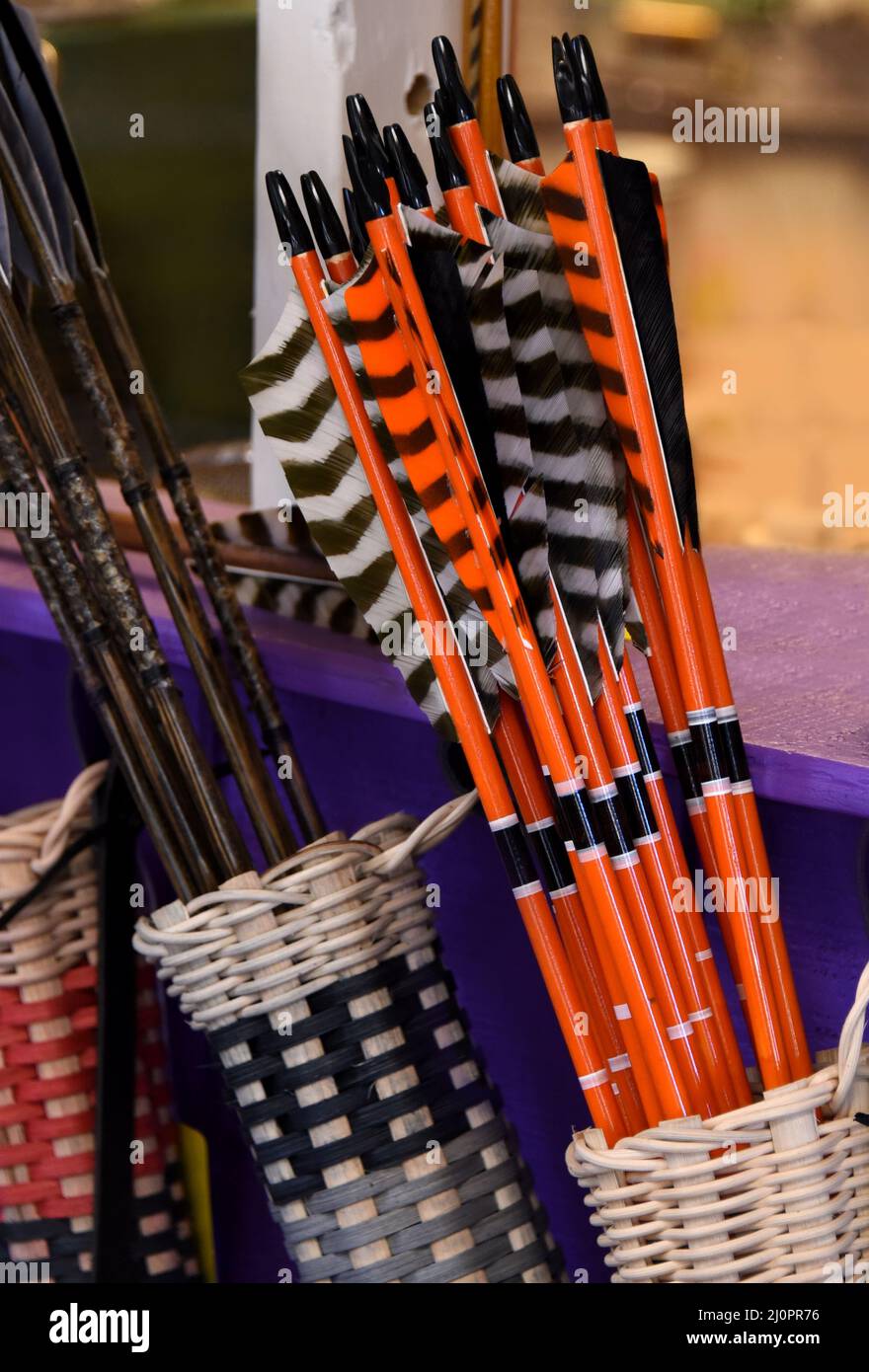 Pfeilhaufen werden in Körben angezeigt. Einige sind schwarz und braun, andere orange und schwarz. Federn sind schwarz und weiß. Stockfoto