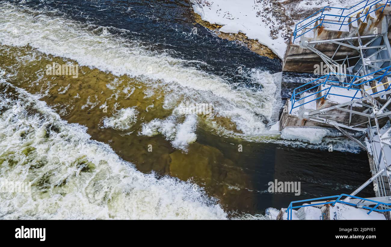 Der Frühling ist nahe, und der starke Schnee schmilzt, da Wasser schnell durch einen Damm fließt Stockfoto