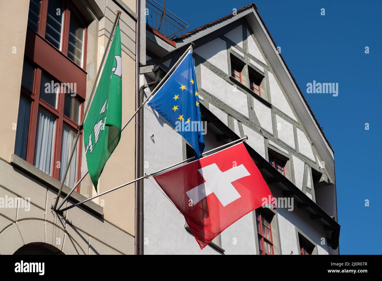 St. Gallen, Schweiz 9. März 2022 Schweizer Flagge und eine europäische Flagge zusammen mit der Flagge des Kantons St. Gallen an der Fassade eines alten Gebäudes Stockfoto