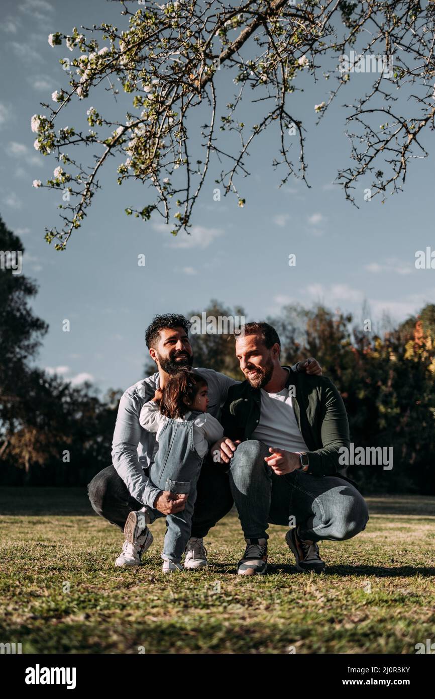 Männlich Gay Paar kümmern sich um ihre kleine Tochter in einem Park. Modernes Familienkonzept. Vertikal. Stockfoto