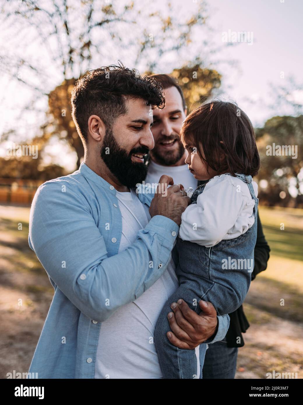 Glücklich männlich Gay Paar mit ihre Tochter in ihren Armen. Ihr Vater gibt ihr den Schnuller. Stockfoto