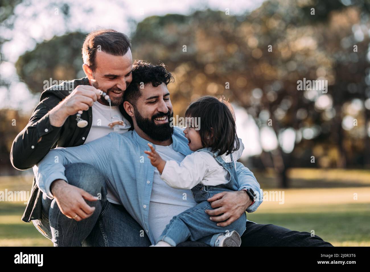 Männlich Homosexuell Familie umarmt und spielt mit ihren kleinen Tochter im Park. Stockfoto