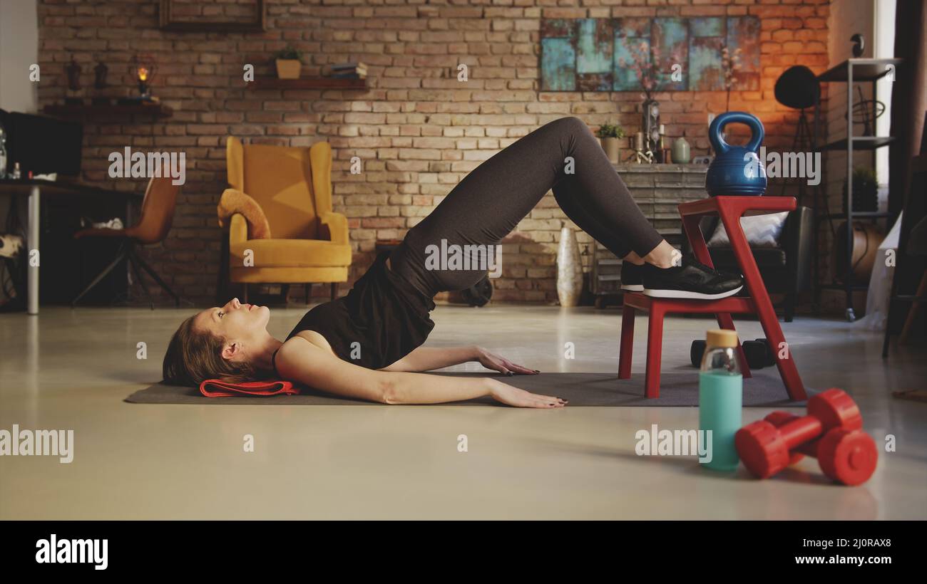 Fitnesstraining zu Hause. Junge Frau macht Bauch-Training, die Ausübung im Wohnzimmer. Bleiben Sie zu Hause und bleiben Sie fit und gesund. Stockfoto