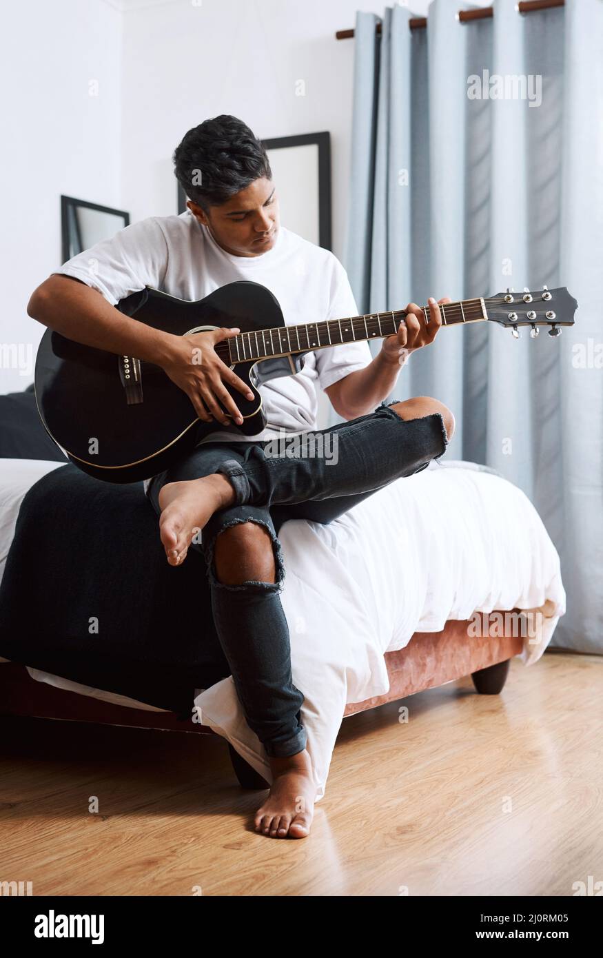 Deshalb bin ich immer im Mittelpunkt. Aufnahme eines jungen Mannes, der Gitarre spielt, während er zu Hause sitzt. Stockfoto