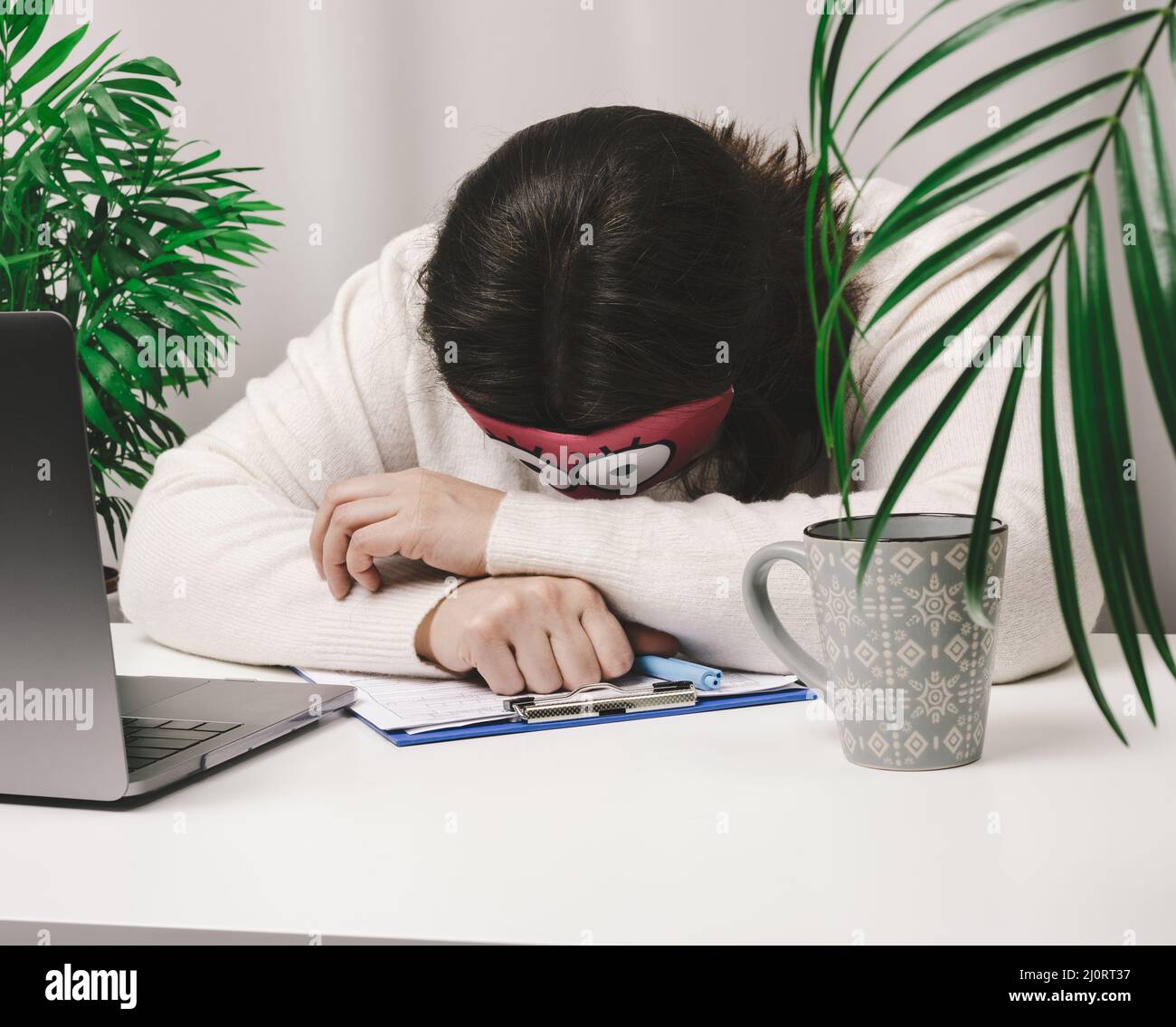 Frau in einem Pullover schläft an einem Arbeitstisch neben einem Laptop. Ermüdung und Überarbeitungs-Konzept. Faulheit Stockfoto