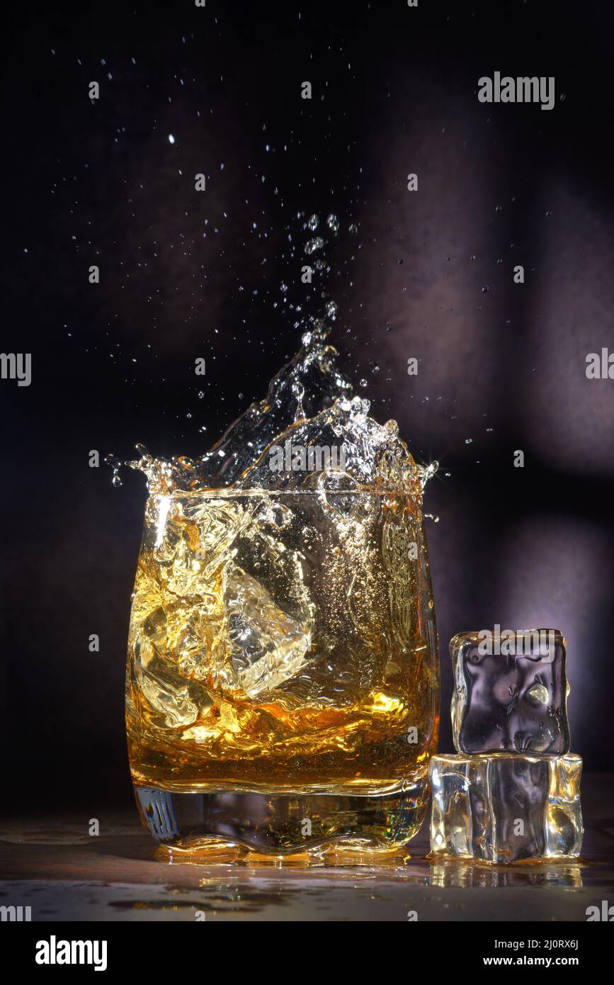Glas alten Whiskys mit Eis. Ein spritzendes Glas Whiskey mit Eis isoliert auf einem dunklen Hintergrund Stockfoto