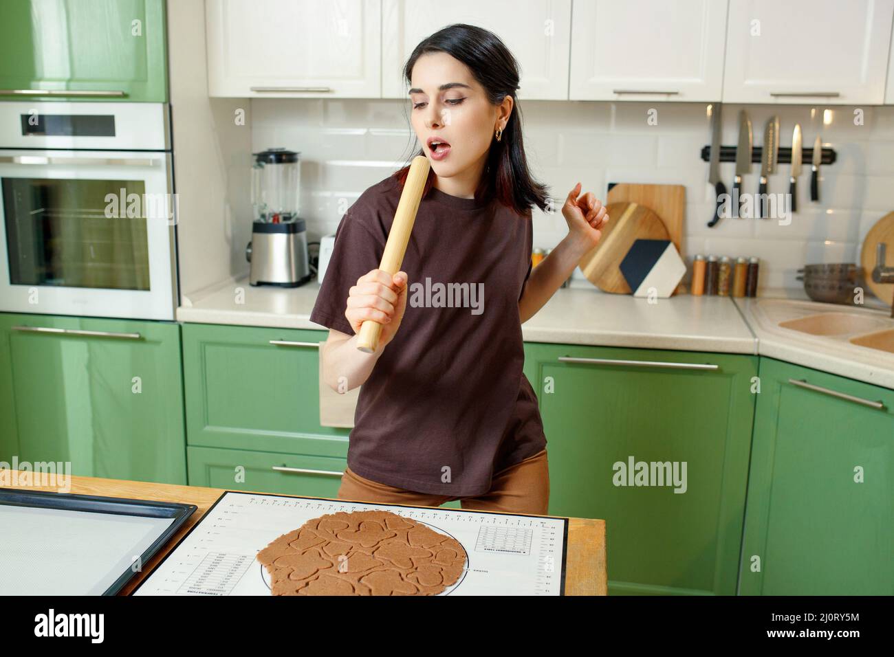 Junge glücklich fröhlich brünette gemischt Rennen Frau Vorbereitung hausgemachte Kekse beim Tanzen. Stockfoto