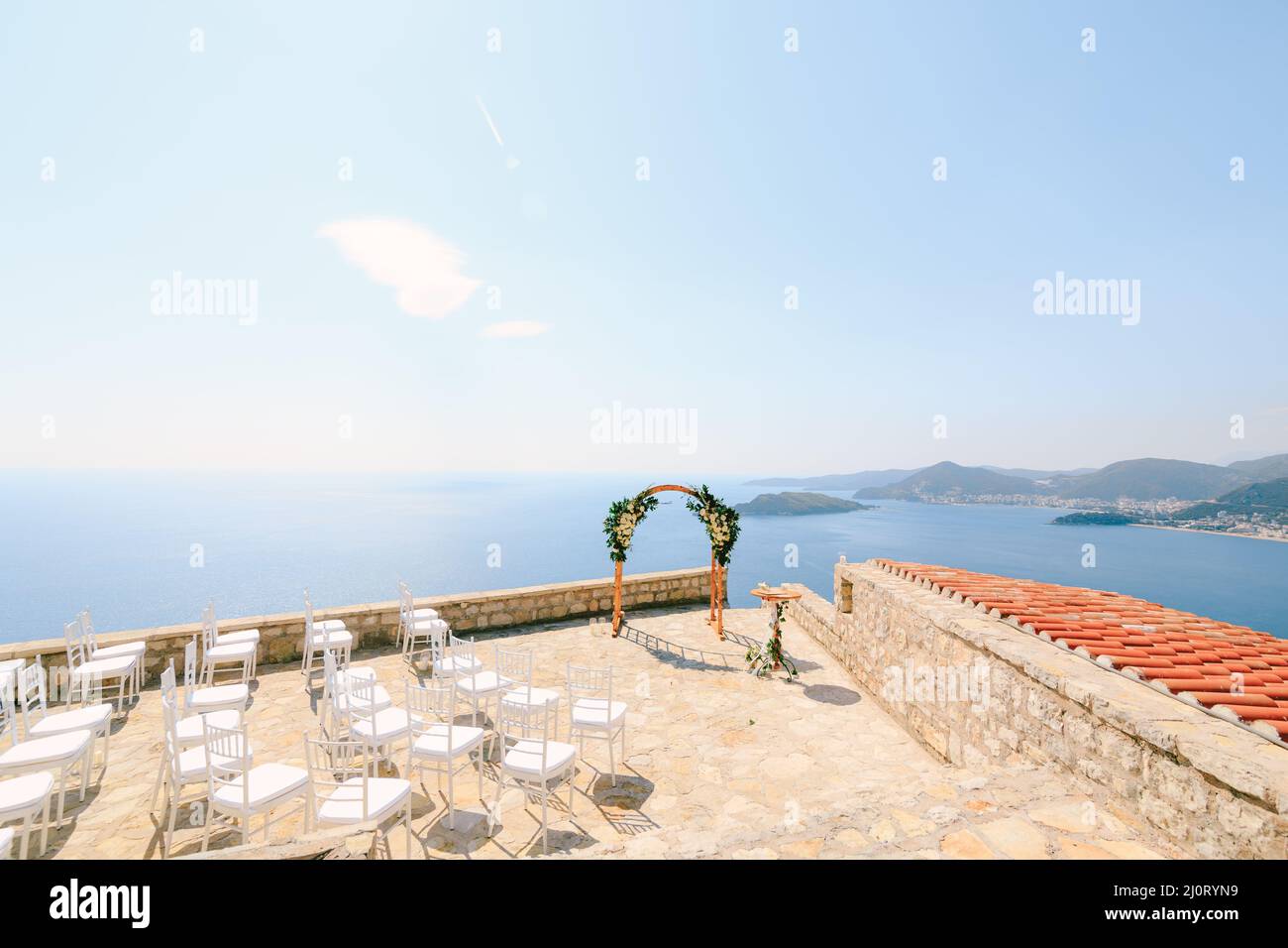 Weiße Stühle stehen vor einem Hochzeitbogen auf einer Aussichtsplattform mit Blick auf das Meer Stockfoto