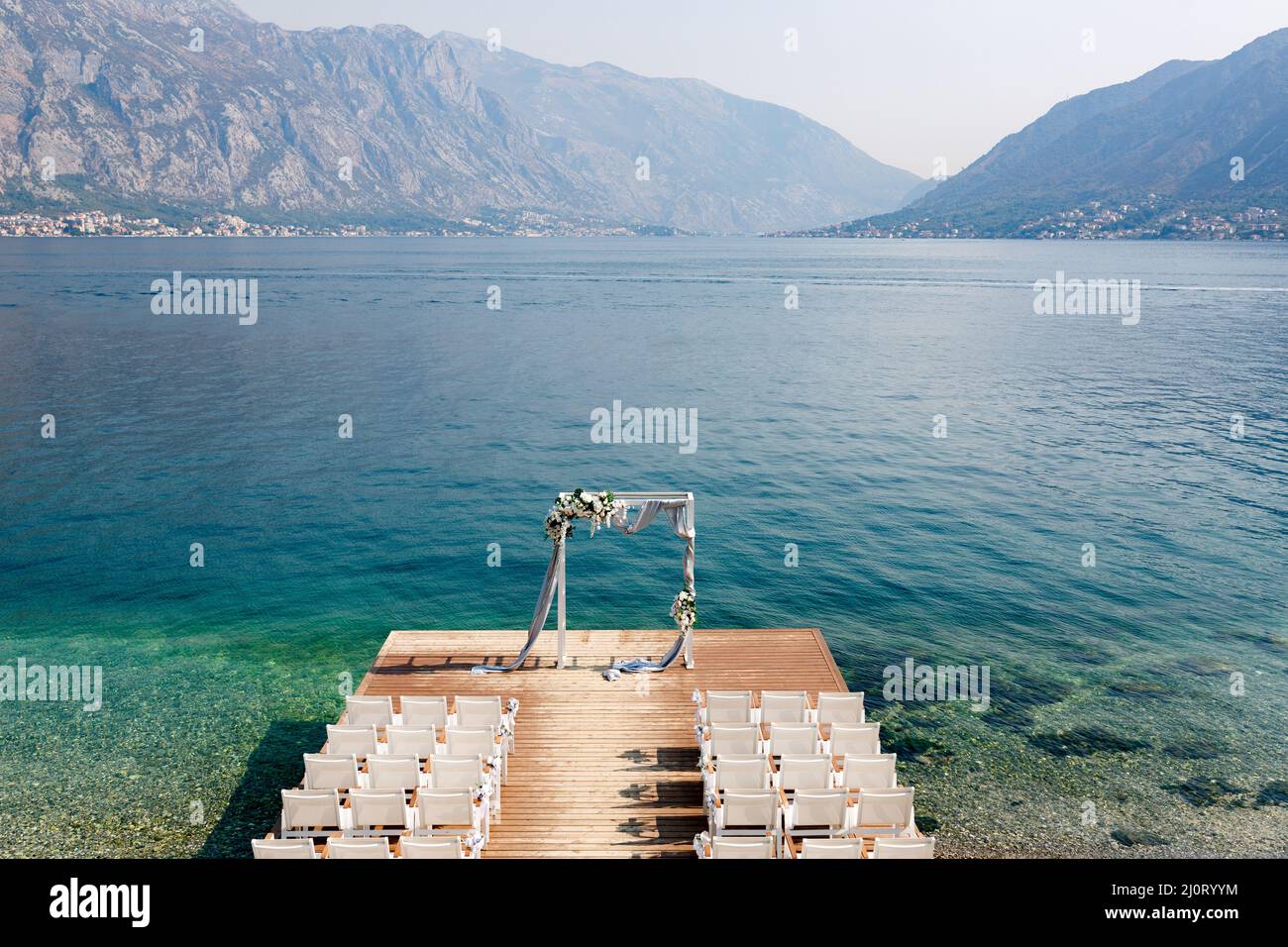 Stühle auf dem hölzernen Pier vor dem Hochzeitsbogen vor dem Hintergrund des Meeres Stockfoto