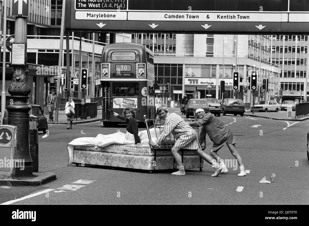 Patricia Hodge wird als Fernsehreporterin Jemima Shore in der neuen Serie "Jemima Shore Enforschungen" von Thames Television zu sehen sein. Im Bild kommt der Verkehr in Londons geschäftigen Tottenham Court Road zum Stillstand, als Patricia Hodge mit zwei der Darsteller der Serie, Larry Lamb und Malcolm Stoddard, ins Bett geht. 5.. Juni 1983. Stockfoto