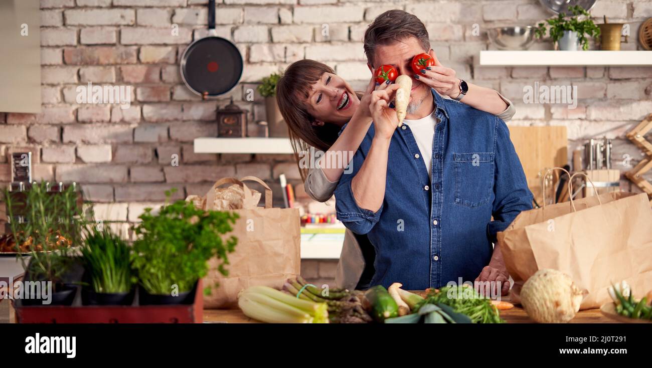 Glückliches Paar in der Küche Auspacken Lebensmittelbeutel voller Gemüse Ankunft nach Hause vom Einkaufen Spaß haben, Schrauben Sie herum. Stockfoto