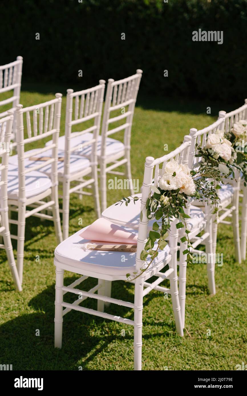 Eine Reihe von weißen Stühlen mit Blumensträußen steht auf einem grünen Rasen Stockfoto
