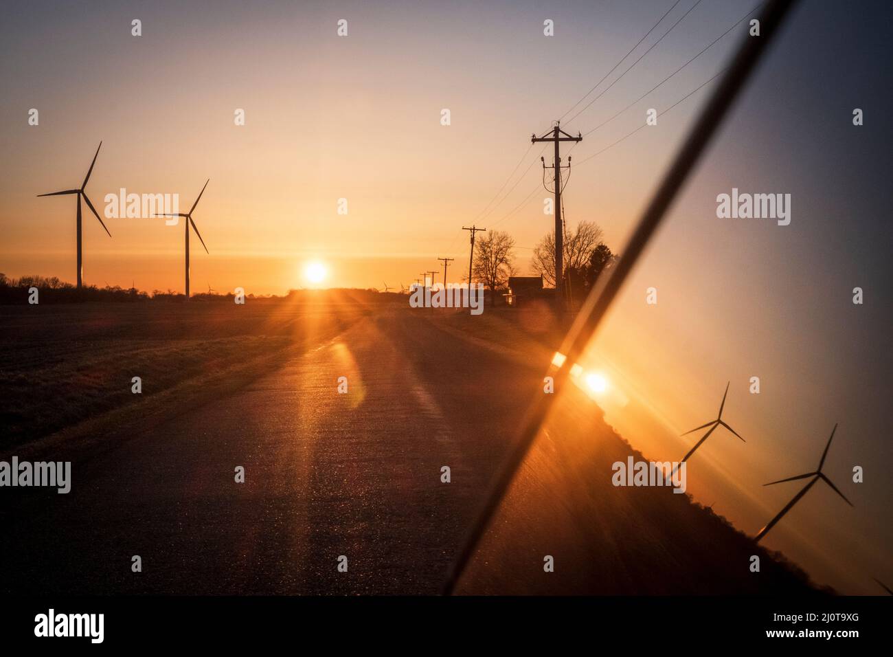 Windturbinen und Telefonmasten entlang einer Landstraße im amerikanischen Mittleren Westen bei Sonnenuntergang Stockfoto