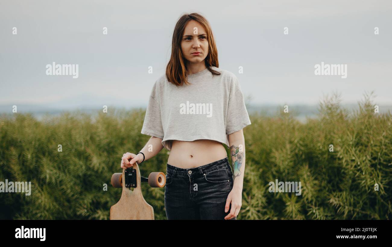 Porträt eines gewöhnlichen Teenagers aus dem Dorf. Das Mädchen hält ein Longboard in der Hand Stockfoto