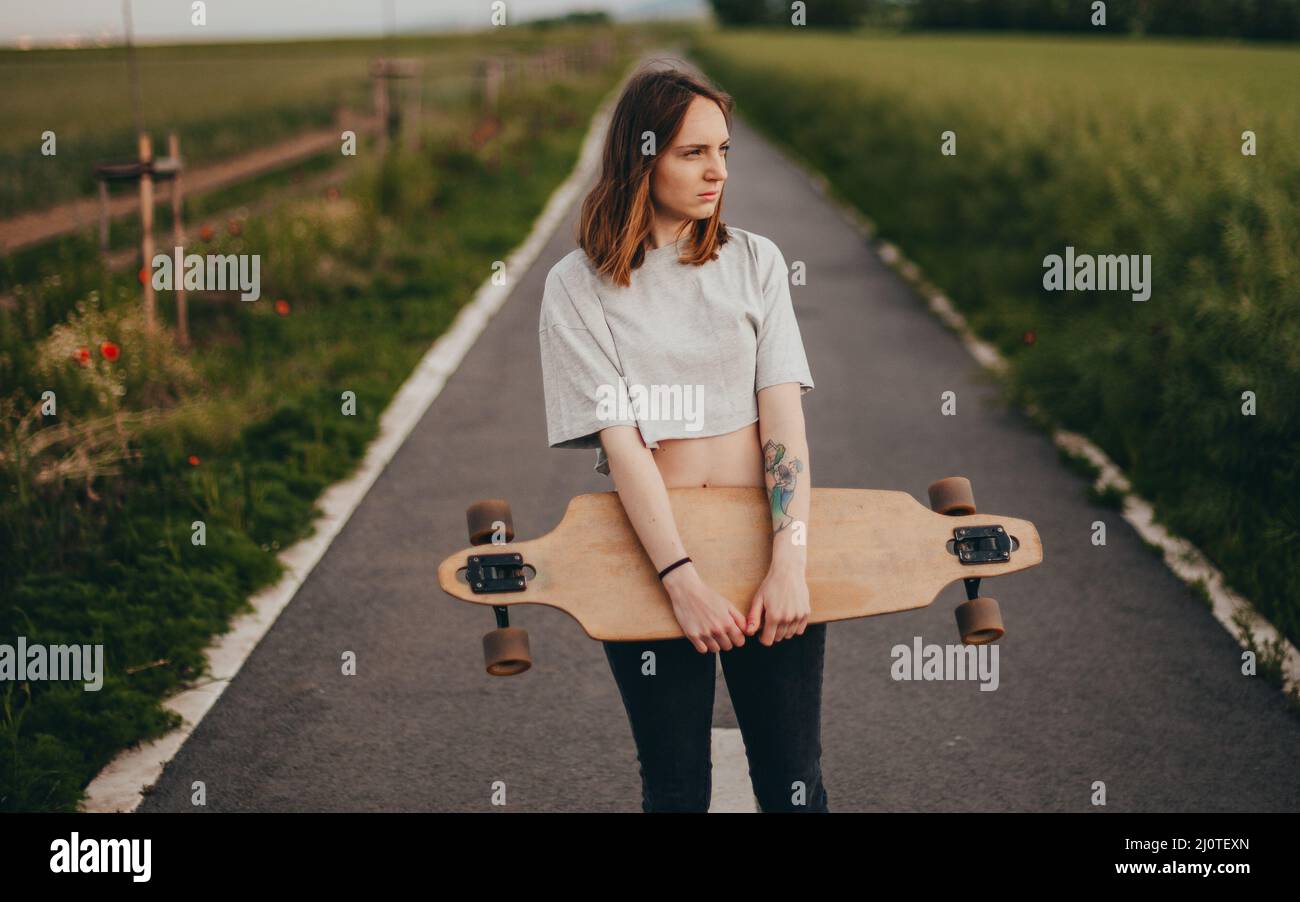 Porträt eines gewöhnlichen Teenagers aus dem Dorf. Das Mädchen hält ein Longboard in der Hand und lächelt Stockfoto