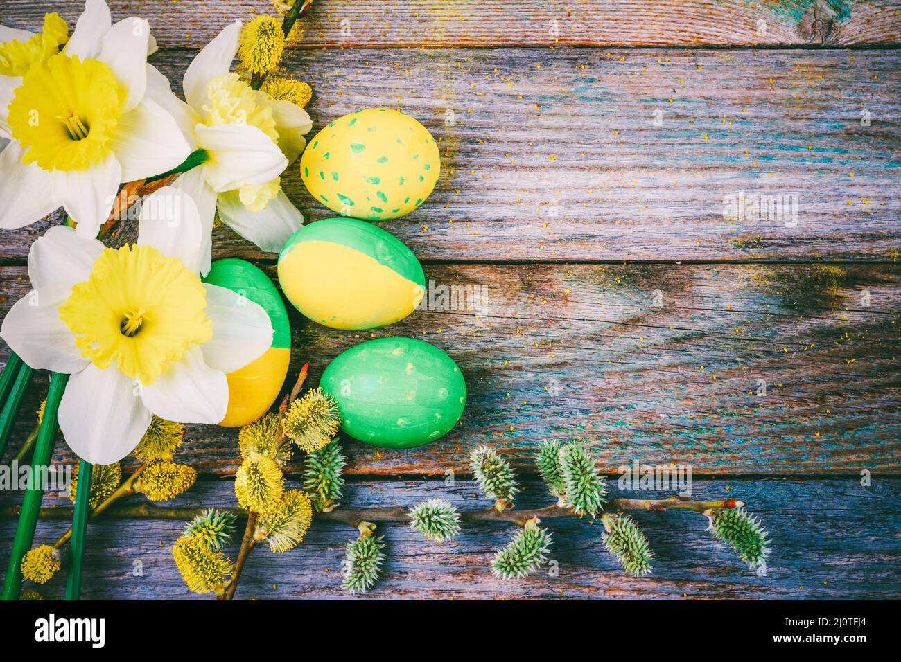 Osterzusammensetzung aus Narzissen blühenden Weidenzweigen und Ostereiern mit einem Muster von gelber und grüner Farbe auf einem Waldstück Stockfoto