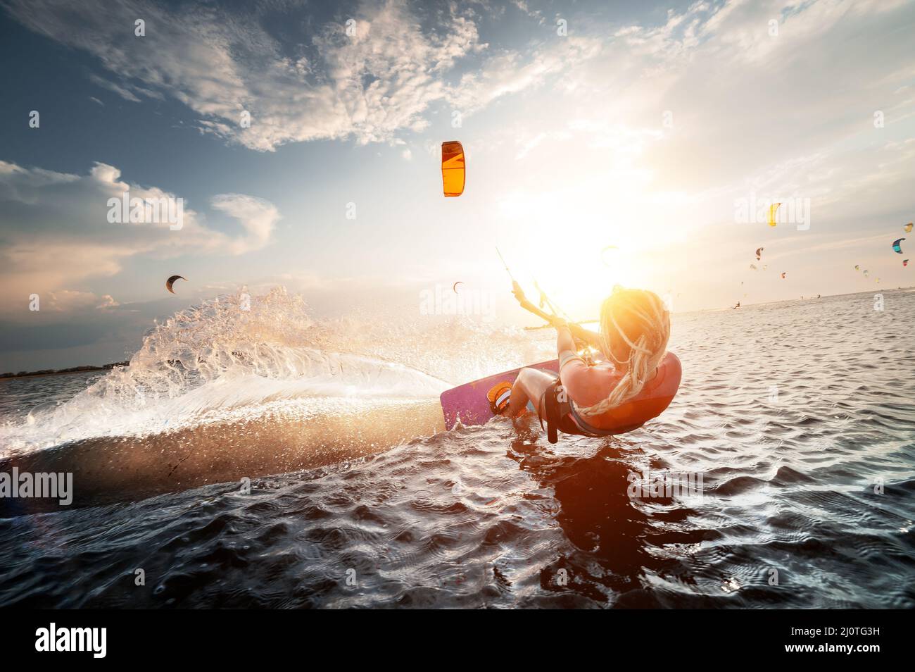 Die professionelle Kite-Surferin Frau reitet auf einem Brett mit einer Planke in den Händen auf einem leman See mit Meerwasser bei Sonnenuntergang. Wasserspritzer Stockfoto