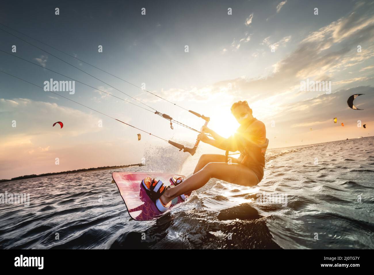 Die professionelle Kite-Surferin Frau reitet auf einem Brett mit einer Planke in den Händen auf einem leman See mit Meerwasser bei Sonnenuntergang. Wasserspritzer Stockfoto