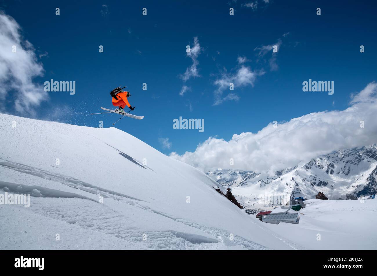 Fliegen in einem Sprung über einen Hang Freestyle Skifahrer springen in einem orangen Skianzug in den verschneiten Bergen an einem sonnigen Tag Stockfoto