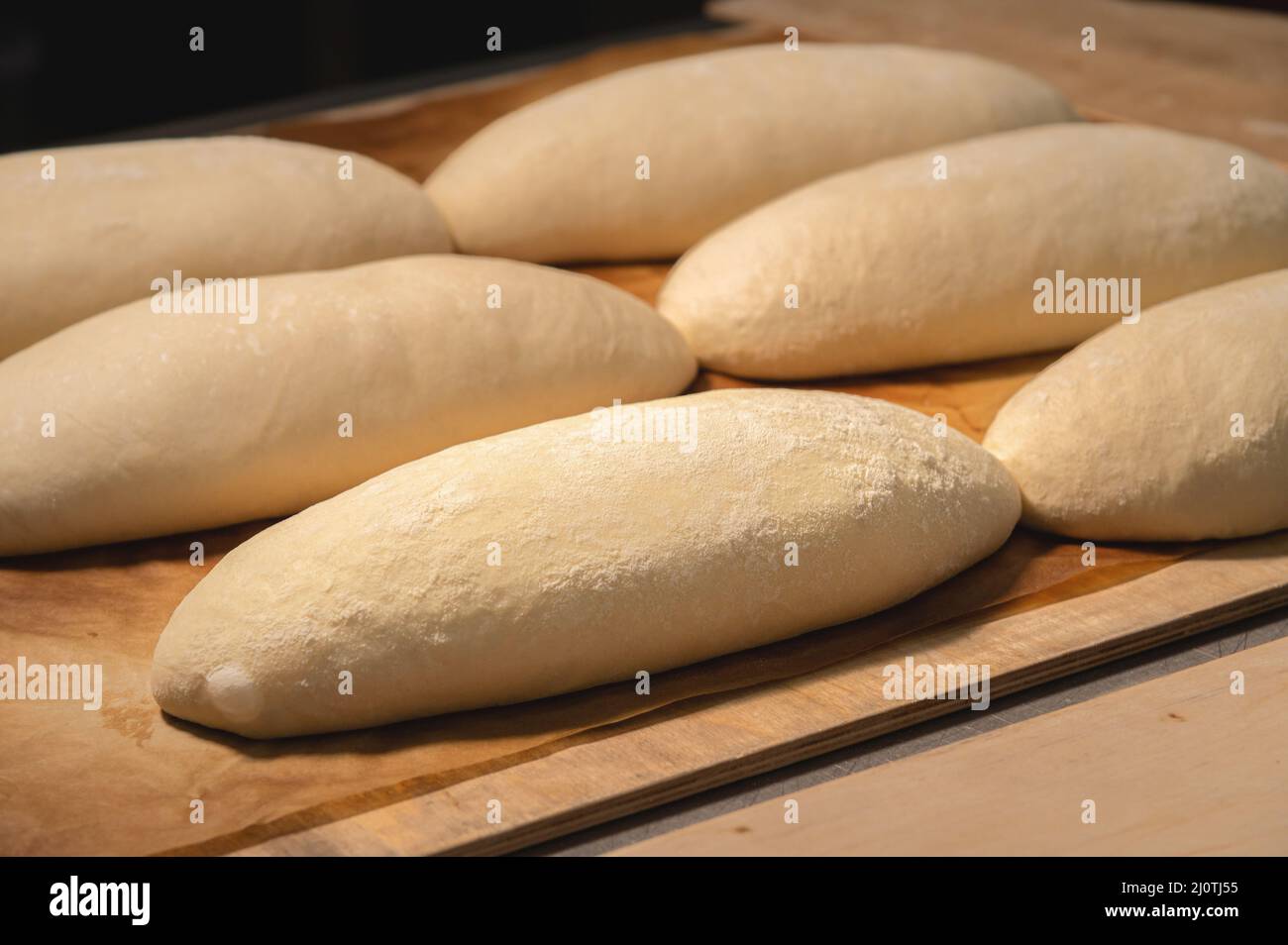 Mehrere Brote rohen Teigs liegen auf einem Holzbrett. Basteln Sie vor dem Backen Brot Stockfoto