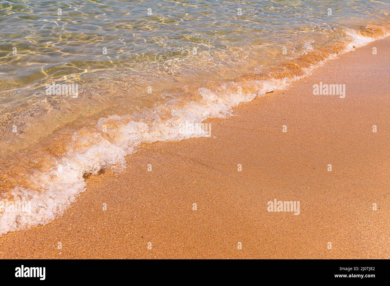 Transparentes Meerwasser. Der goldene Sand wird von kleinen Wellen klaren Wassers mit Schaum gewaschen. Meereshintergrund. Tourismus und Reisen Stockfoto