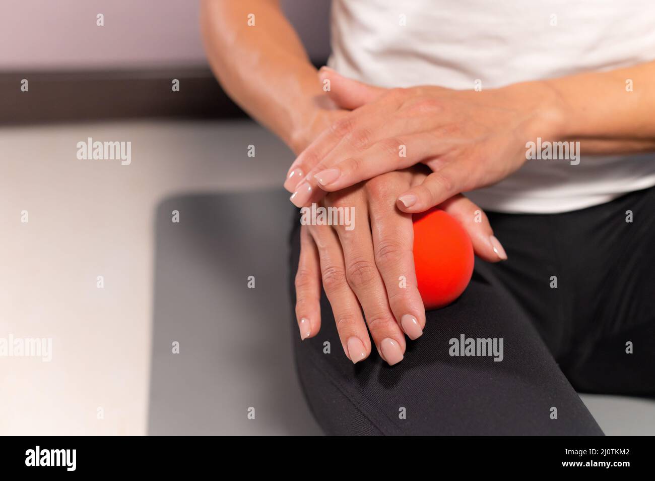 Sportliche schlanke kaukasische Frau bei der Selbstmassage des Oberschenkels auf der Fitnessmatte mit Massageball im Innenbereich. Massage zur Selbstisolierung Stockfoto