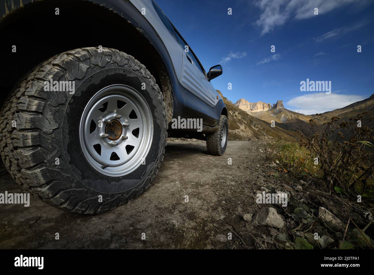 Ein großes SUV-Autorad mit großem Schlamm-Profil steht auf einer felsigen Straße vor dem Hintergrund der Berge. Fahren Sie mit einem Geländefahrzeug Stockfoto