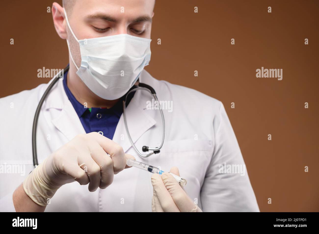 Ein junger weißer kaukasischer Arzt in einem Mantel und einer Maske nimmt einen Impfstoff aus einer Ampulle in eine Spritze. Konzentrieren Sie sich auf die Spritze Stockfoto