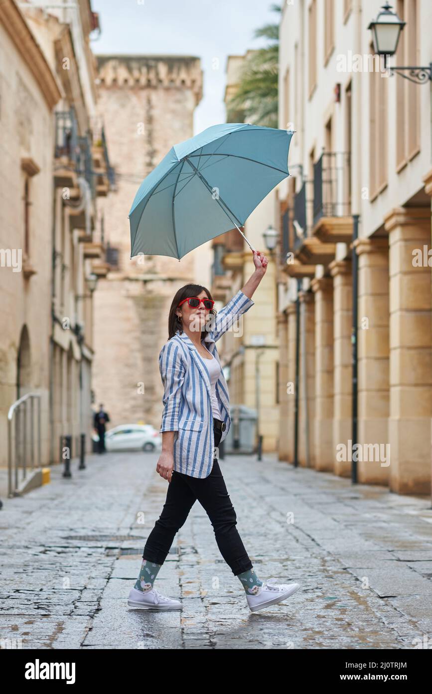 Frau, die an einem regnerischen Tag mit Regenschirm die Straße entlang läuft Stockfoto