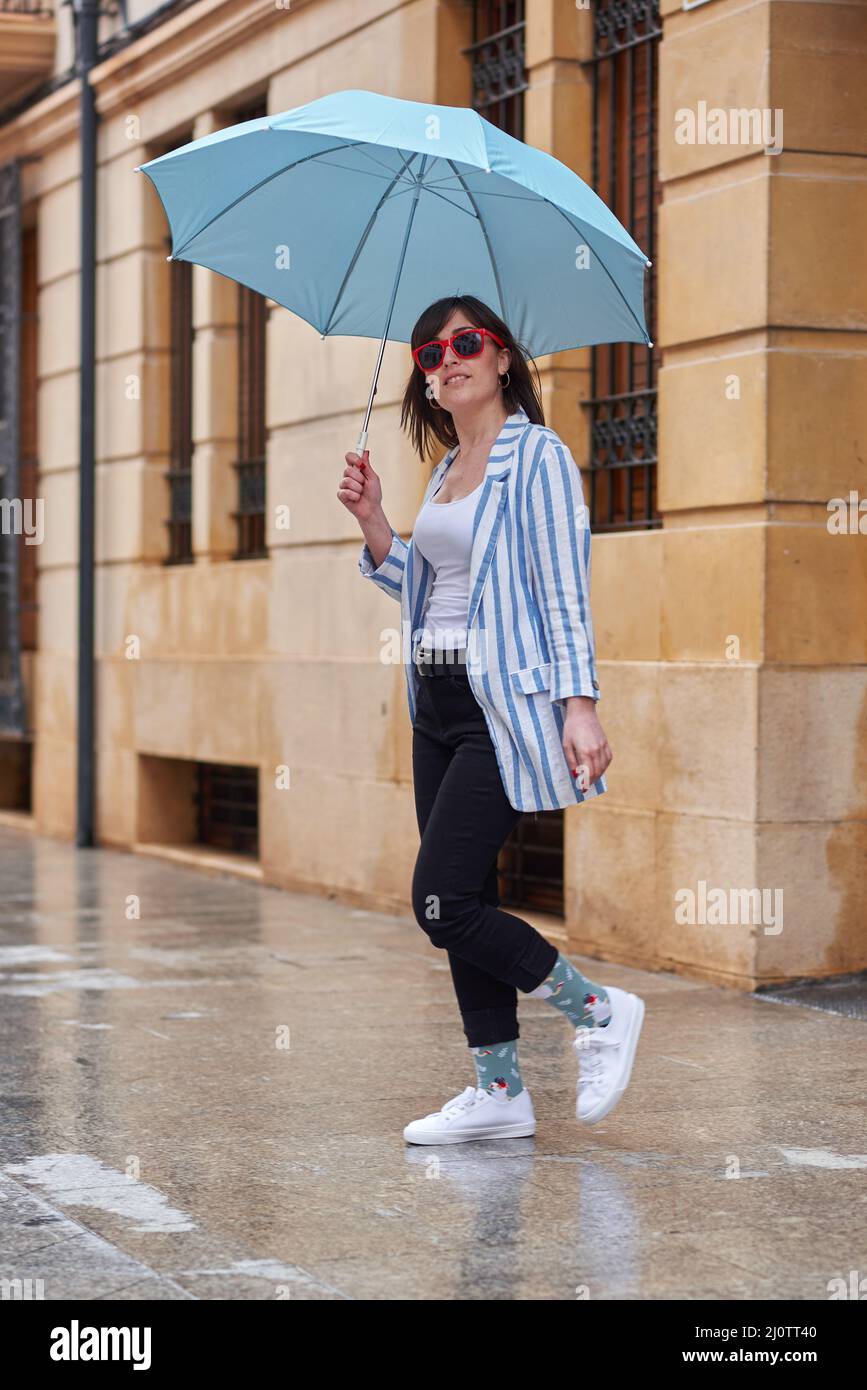 Frau, die an einem regnerischen Tag mit Regenschirm die Straße entlang läuft Stockfoto