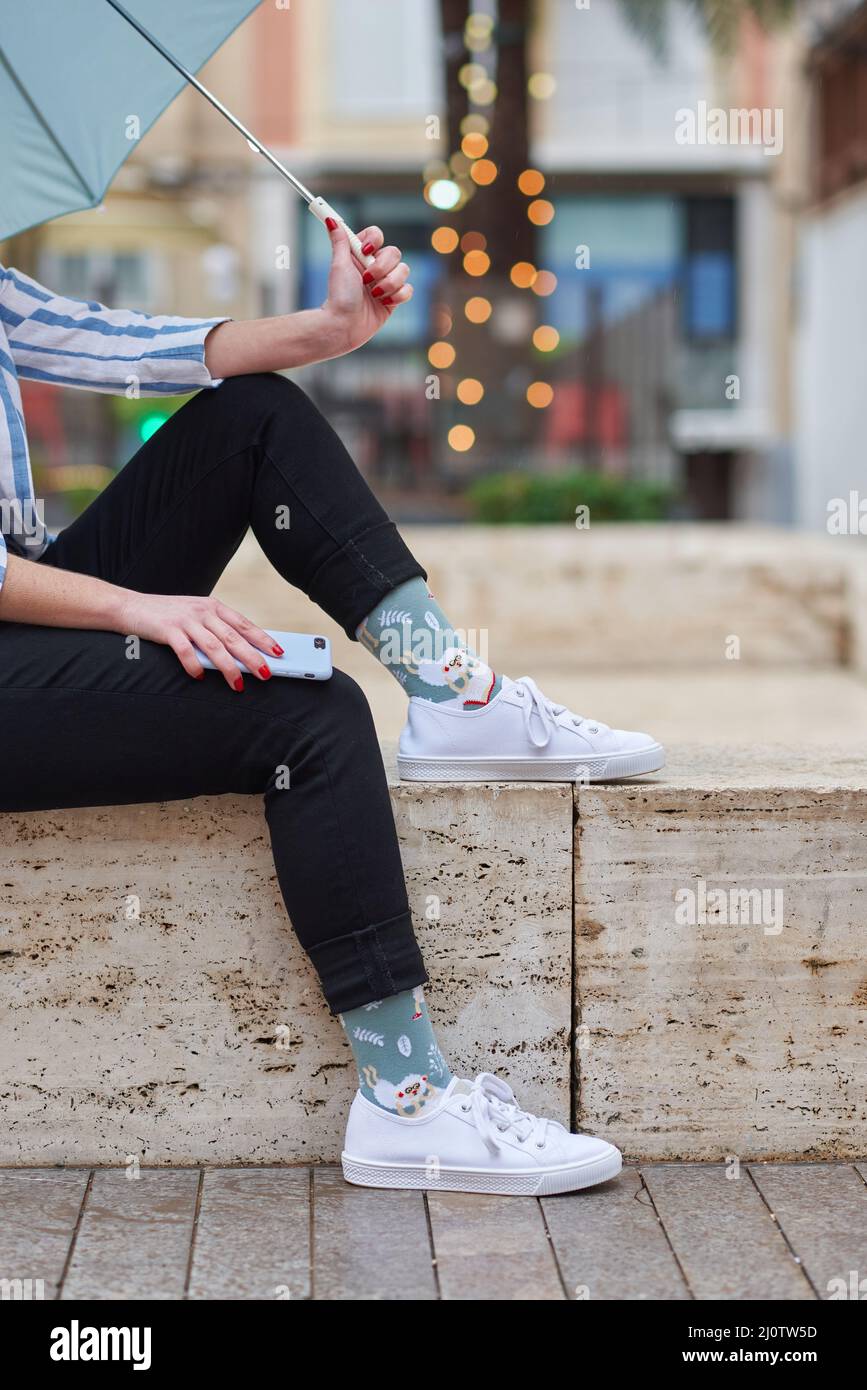 Unkenntliche Frau in lustigen Socken, die im Regen sitzt Stockfoto