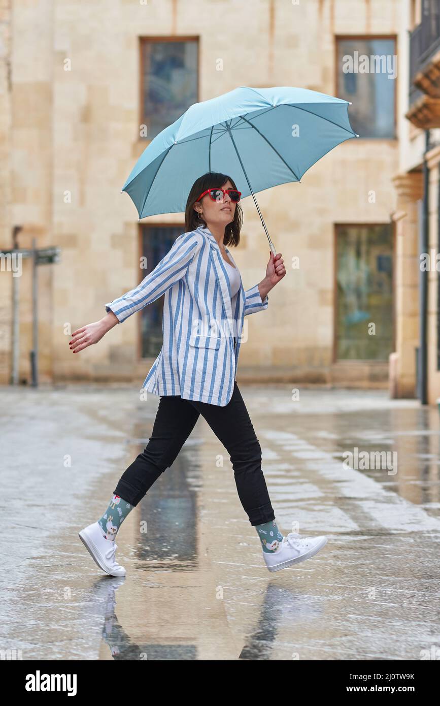 Frau, die an einem regnerischen Tag mit Regenschirm die Straße entlang läuft Stockfoto