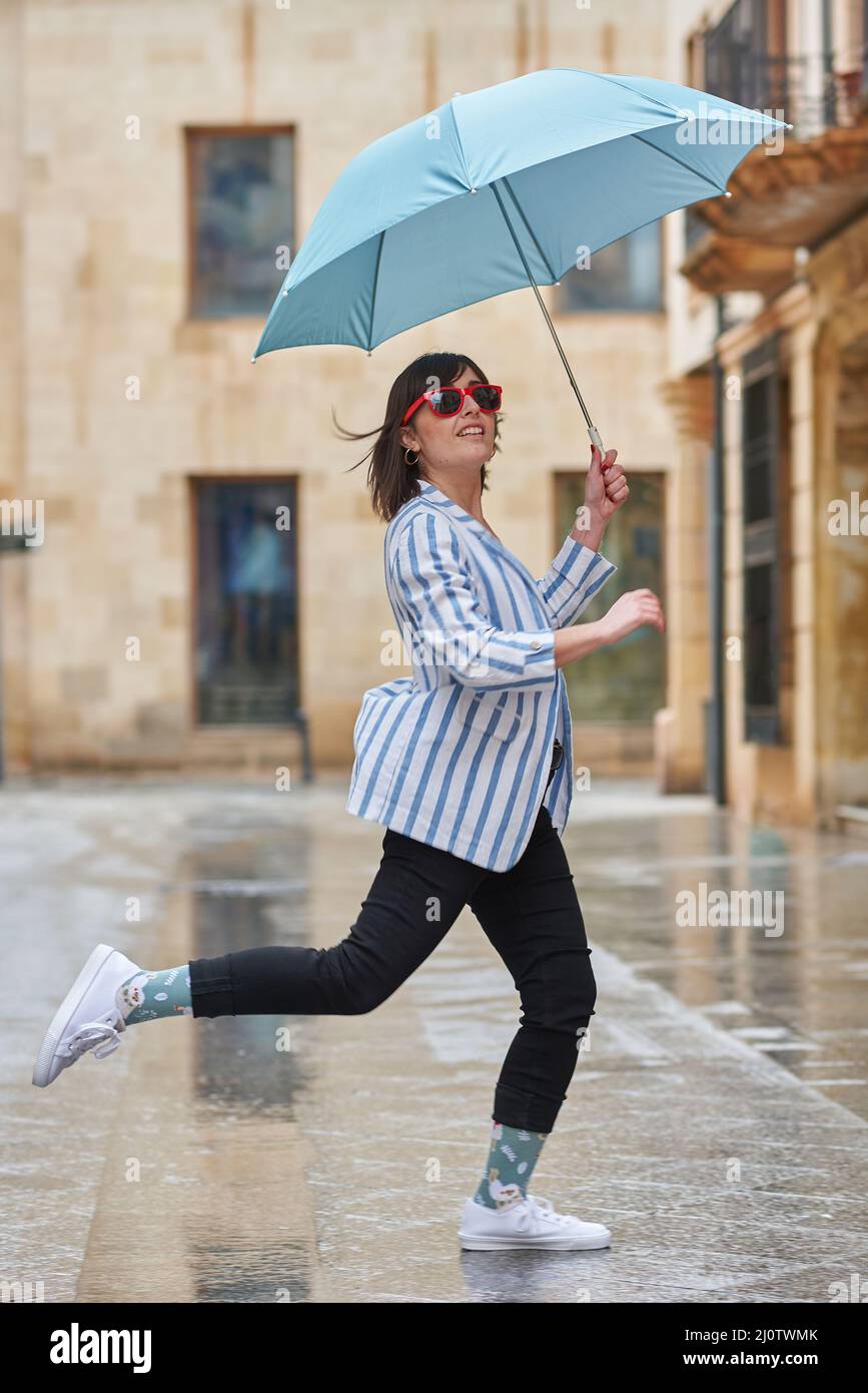 Frau, die an einem regnerischen Tag über eine Pfütze springt Stockfoto