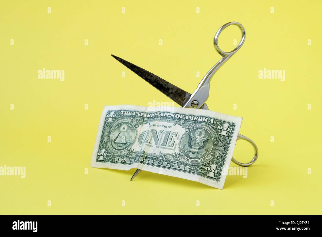 Einen Dollar mit einer Schere auf gelbem Hintergrund schneiden Stockfoto