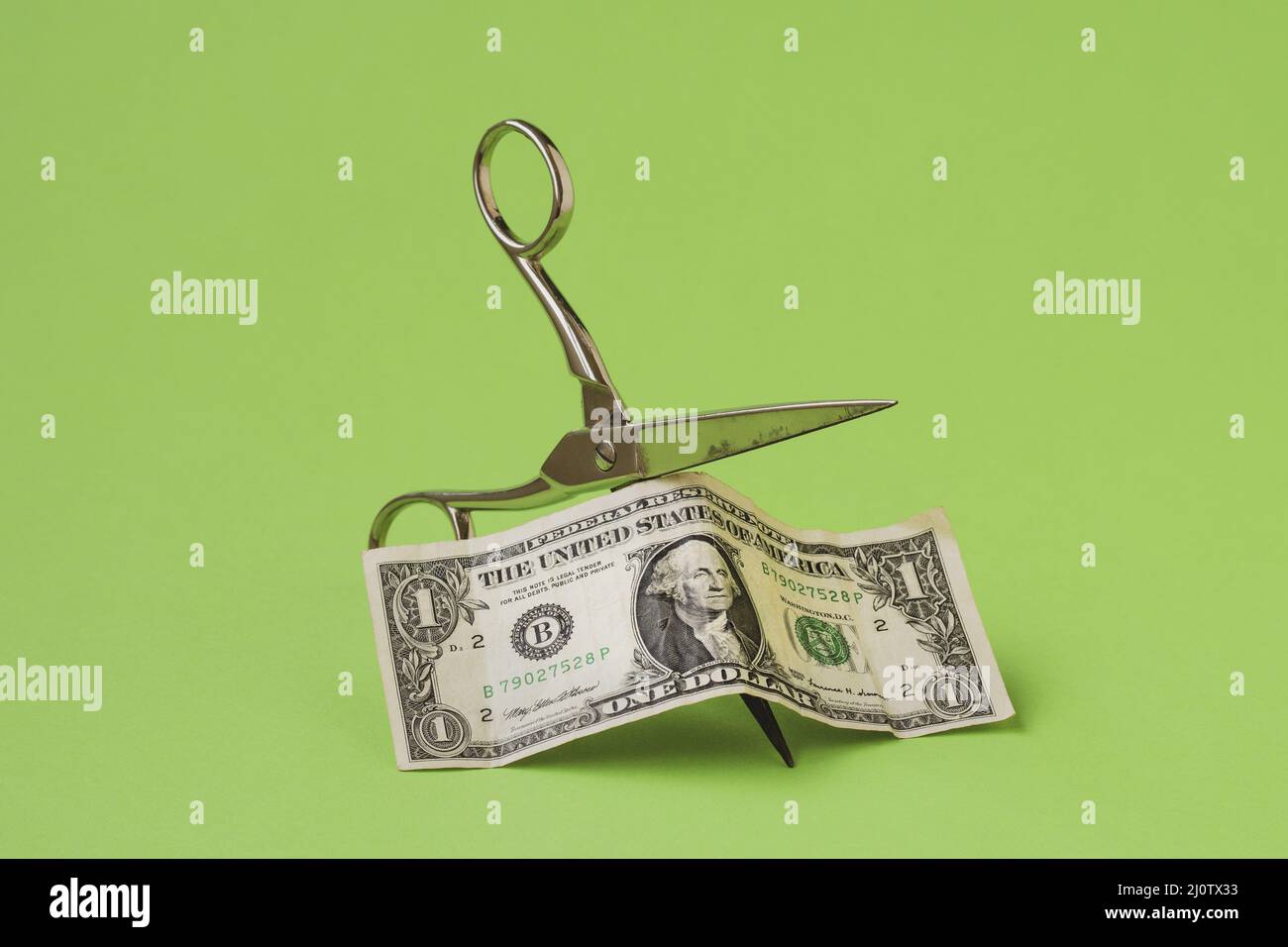 Schneiden Sie einen Dollar mit einer Schere auf grünem Hintergrund Stockfoto