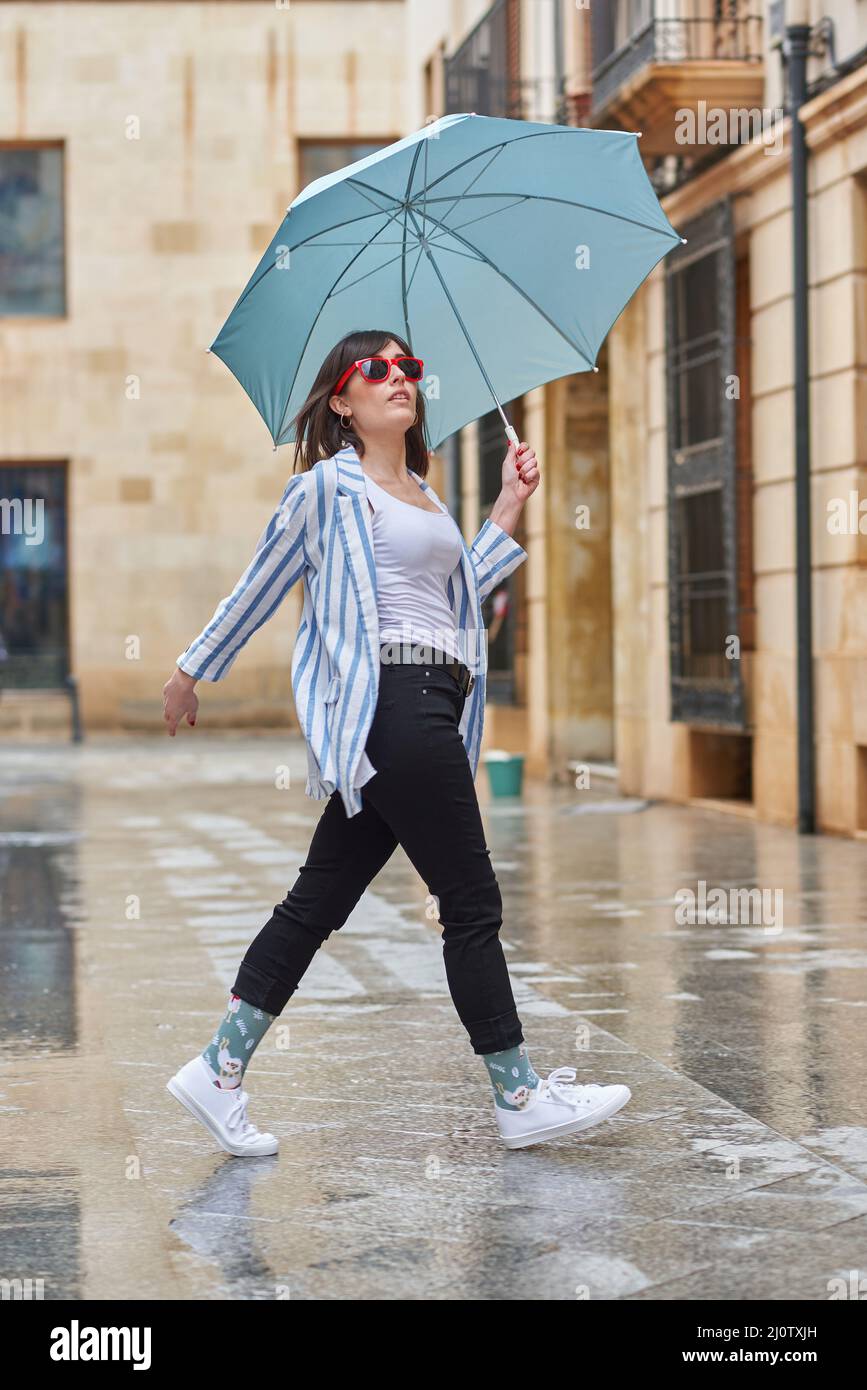 Frau, die an einem regnerischen Tag mit Regenschirm die Straße entlang läuft Stockfoto