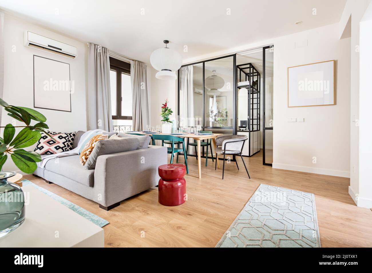 Wohnzimmer mit schmalen weißen Teppichen, grauen Sofas, einem Esstisch aus Holz und einer schwarzen Metall- und Glaswand im Schlafzimmer mit hellem Holzfußboden Stockfoto