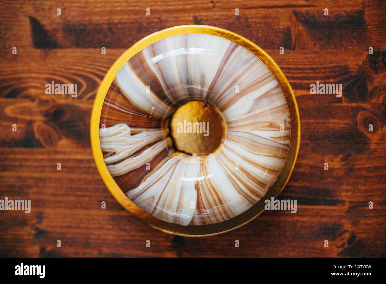 Runder Mousse-Kuchen mit Marmorvereisung auf einem Goldteller auf dem Tisch. Draufsicht Stockfoto