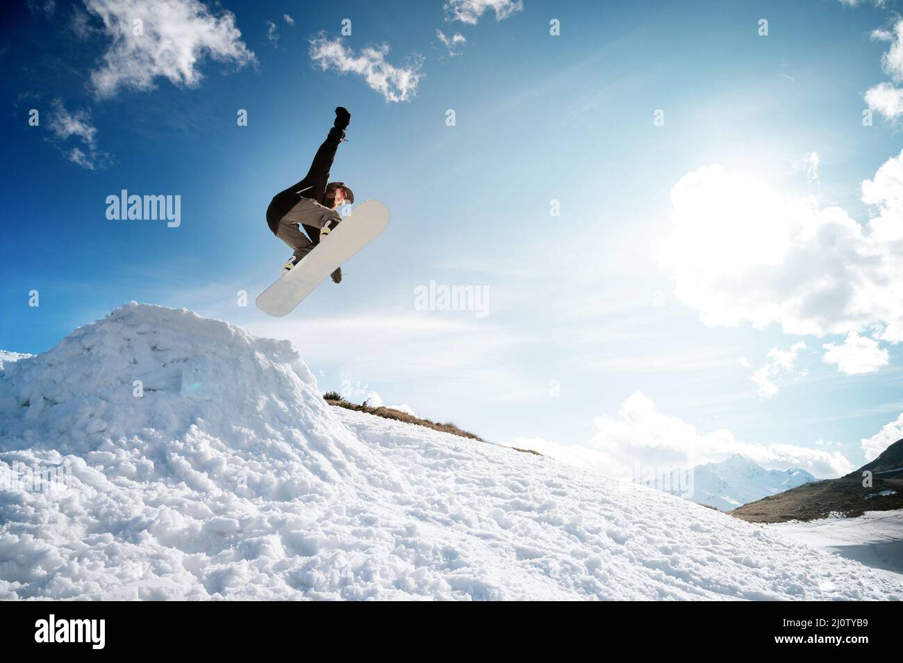 Stilvolle junge Mädchen Snowboarder tut den Trick in Springen aus einem Schneekicker gegen den blauen Himmel Wolken und Berge in der spr Stockfoto