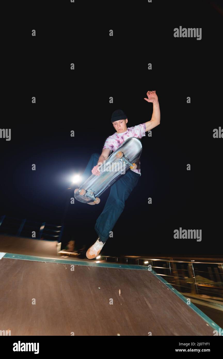 Ein junger Skater macht den Trick, nachts in einem Skatepark zu rutschen. Das Konzept der Nachtruhe und Jugendkultur bei Nacht Stockfoto