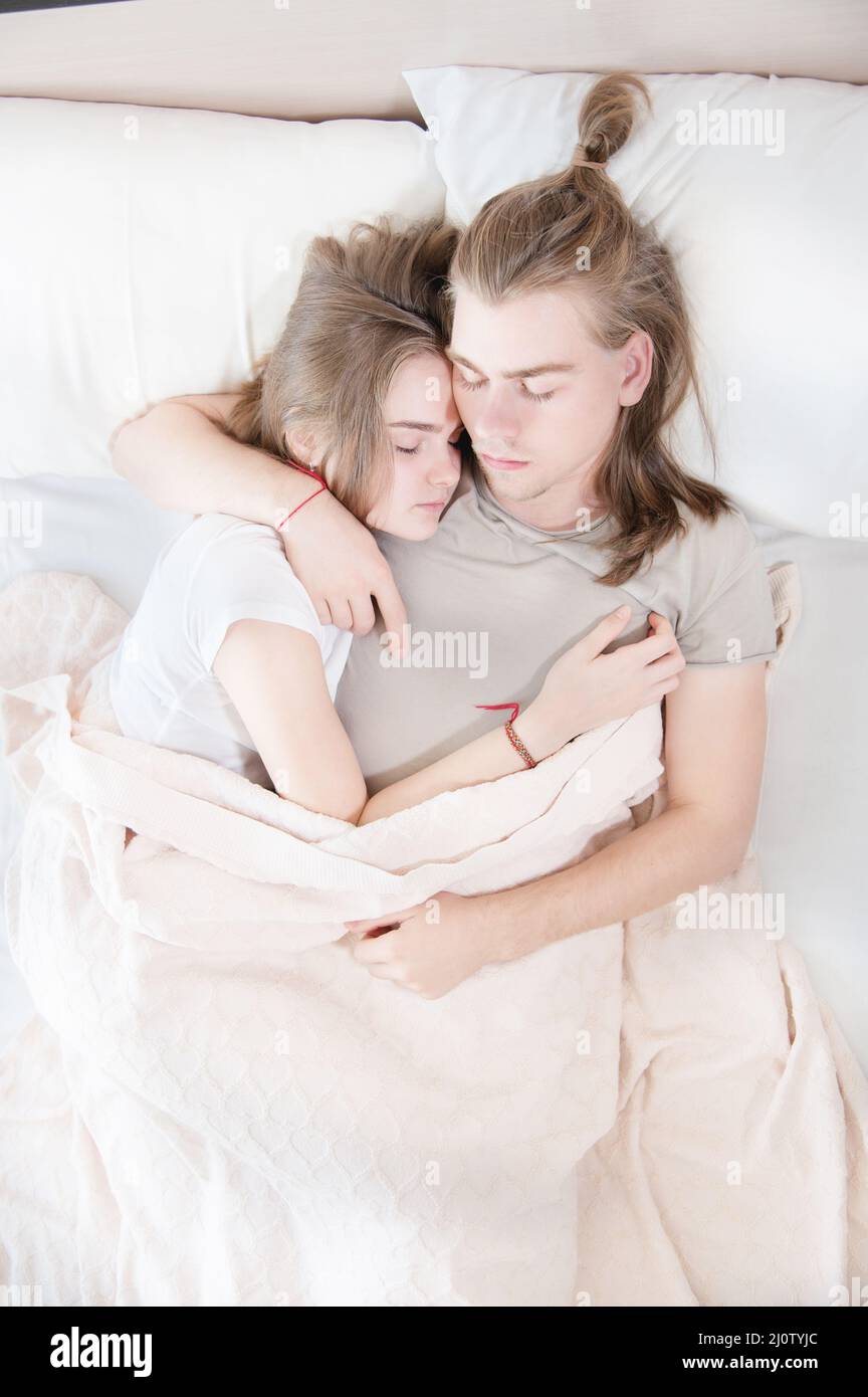 Ein junges Paar moderner Männer und Frauen schlafen in ihrem weißen Bett in einer Umarmung. Das Konzept einer jungen modernen Familie und Schlafprobleme Stockfoto