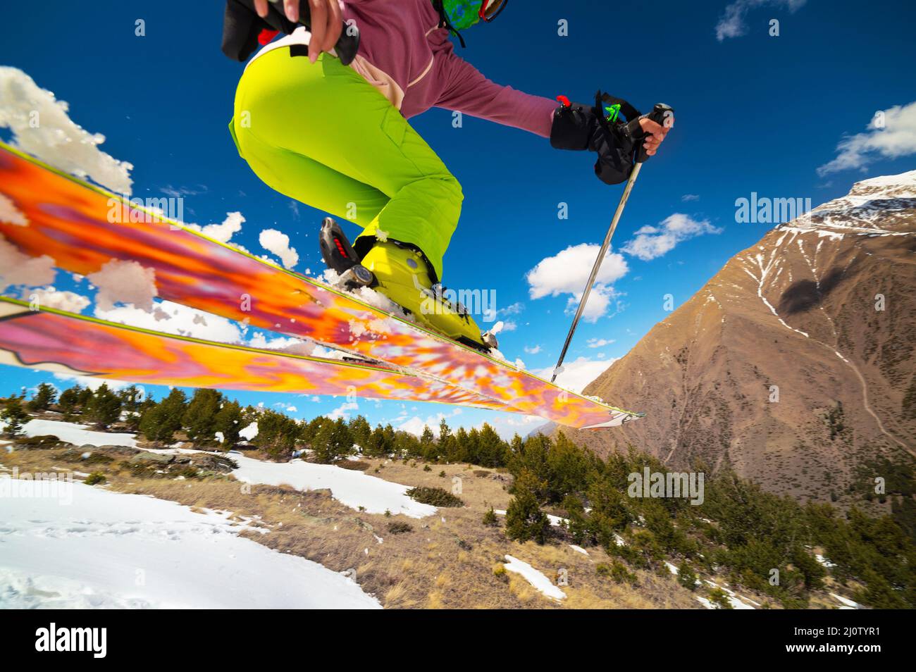 Mädchen Skifahrerin im Flug, nachdem sie im Frühling von einem Kicker vor dem Hintergrund von Bergen und blauem Himmel gesprungen war. Nahaufnahme weit Stockfoto