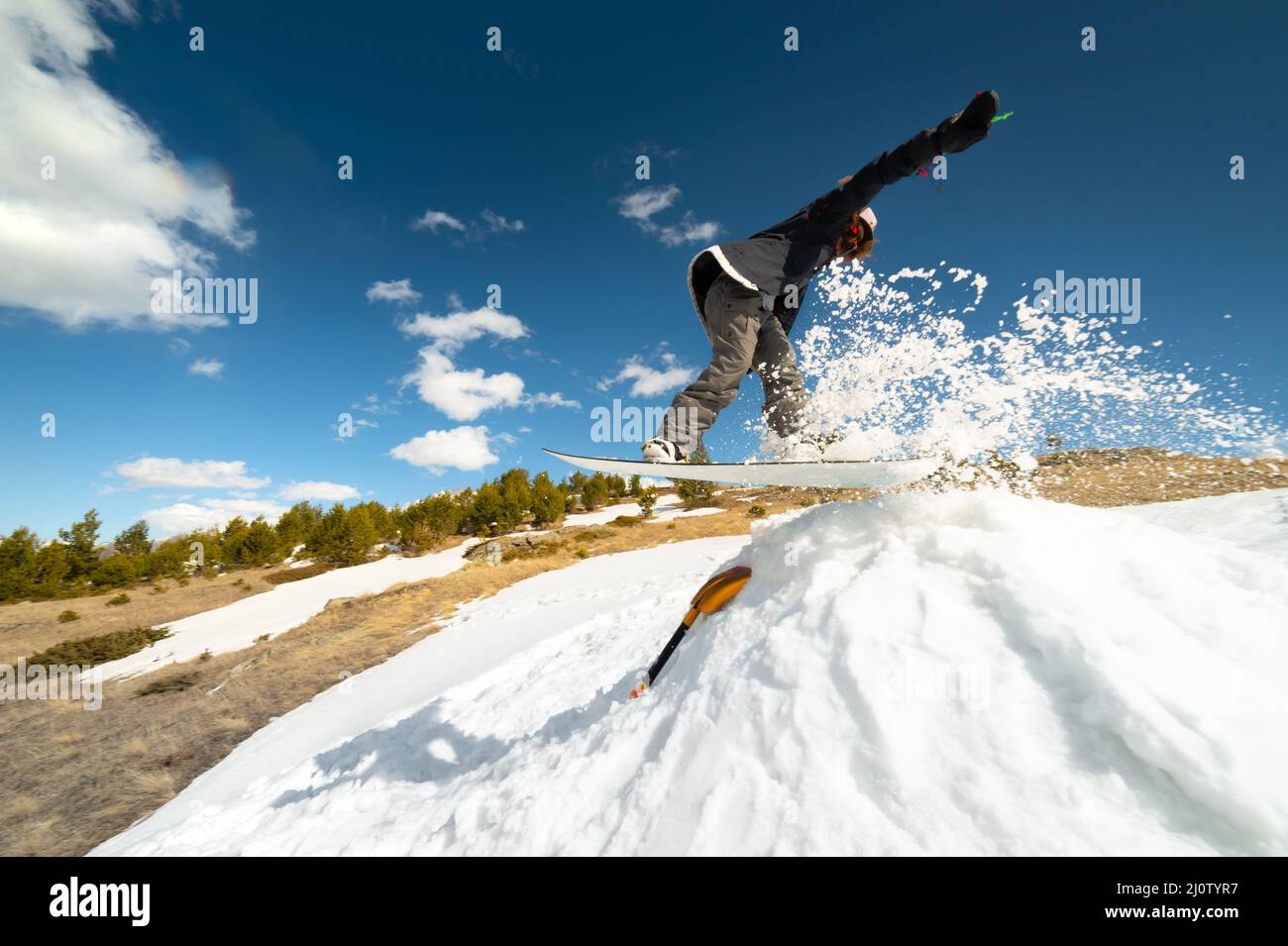 Stilvolle junge Mädchen Snowboarder tut den Trick in Springen aus einem Schneekicker gegen den blauen Himmel Wolken und Berge in der spr Stockfoto