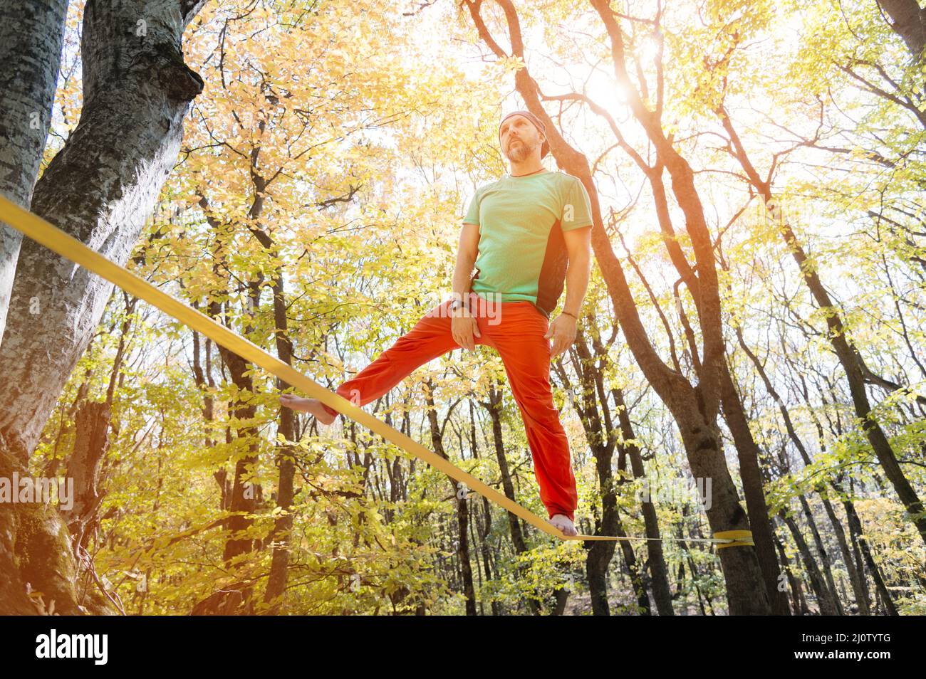 Ein bärtiger Mann im Alter geht an einem sonnigen Nachmittag entlang einer Slackline im Herbstwald. Das Konzept der Freizeit und Erholung von A Stockfoto